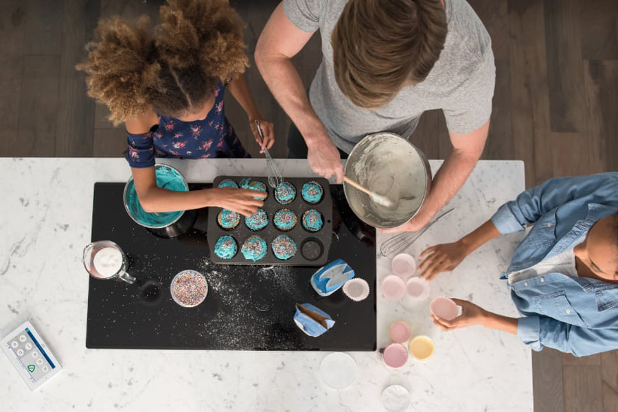 family baking cupcakes with an ADT monitor on the counter.